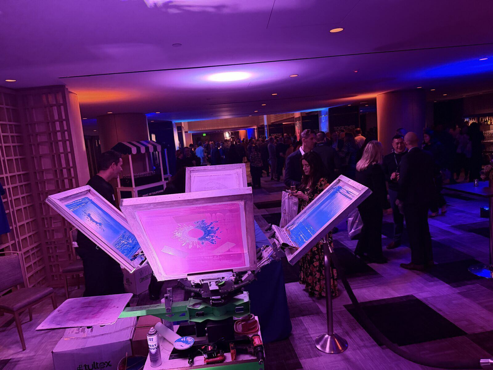 Four-color press printing custom designs at a purple-lit corporate reception